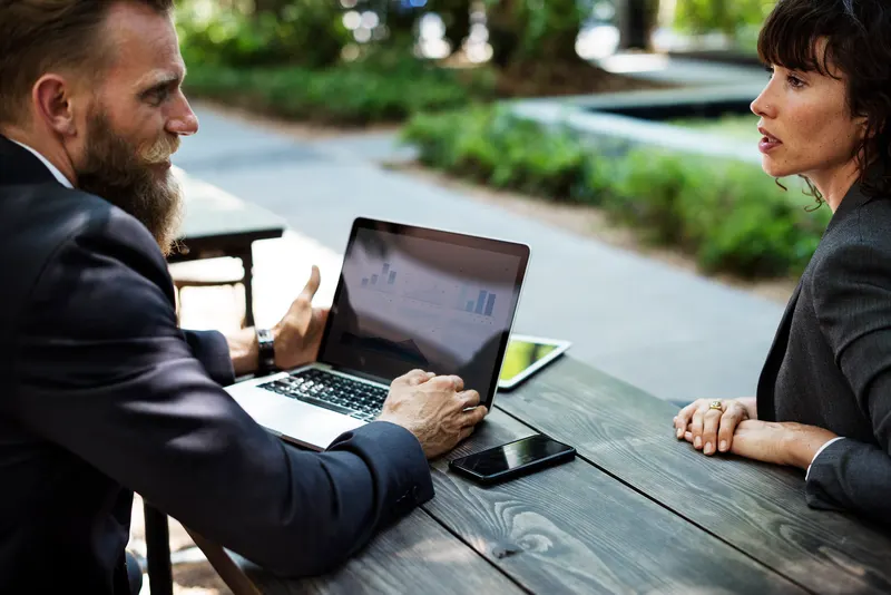 Two people comparing telecom service documents across a conference table